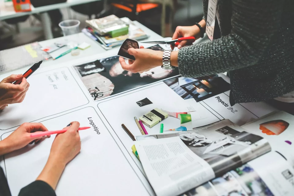 Femme découpant un papier au dessus d'un bureau rempli de feuilles et stylos