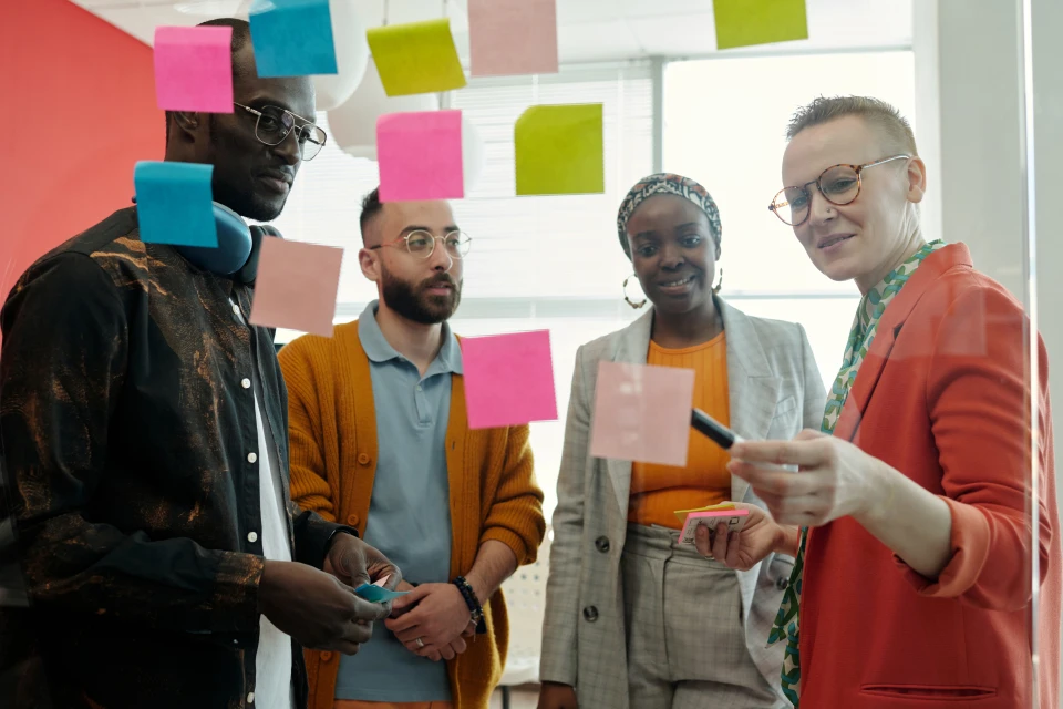 4 personnes debout brainstorment avec des post it sur une vitre transparente