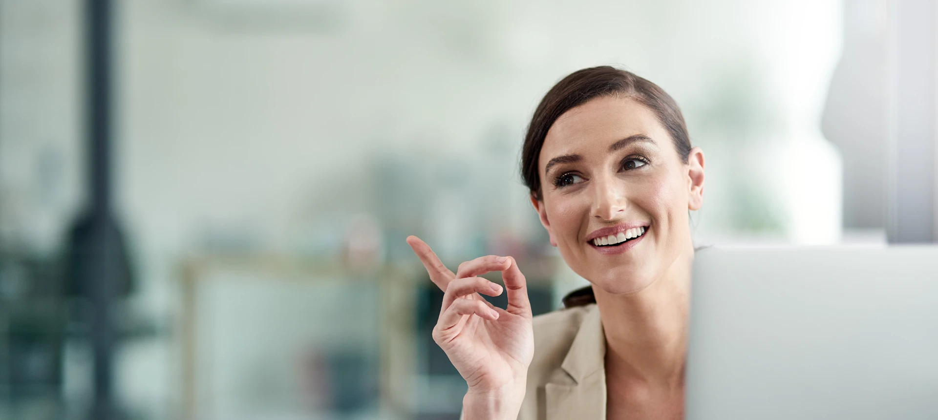 Une femme devant son ordinateur en train de sourire avec le bras accoudé au bureau et l'index pointant en l'air